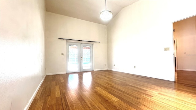 empty room with wood-type flooring, high vaulted ceiling, and french doors