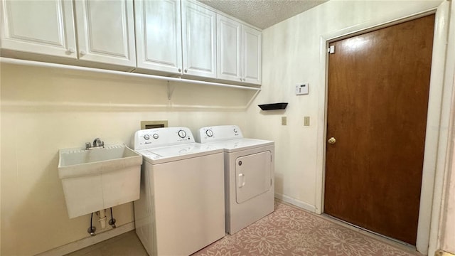 clothes washing area with cabinets, a textured ceiling, washer and dryer, and sink