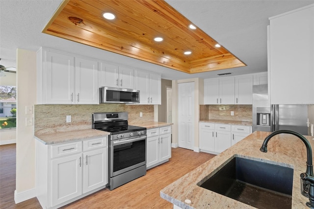 kitchen featuring light wood-type flooring, white cabinetry, stainless steel appliances, and a tray ceiling