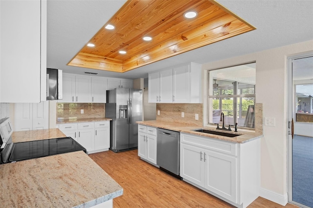 kitchen with stainless steel appliances, sink, light wood-type flooring, a raised ceiling, and white cabinetry