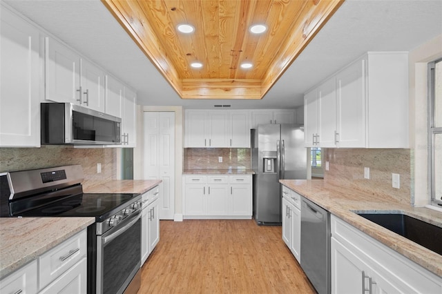 kitchen with white cabinets, a raised ceiling, light stone countertops, light hardwood / wood-style floors, and stainless steel appliances