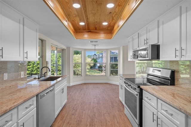 kitchen with light hardwood / wood-style flooring, stainless steel appliances, white cabinets, and a raised ceiling