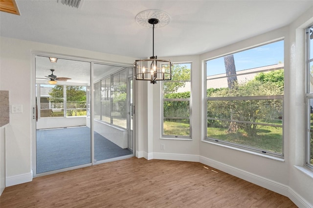 unfurnished dining area featuring a wealth of natural light, ceiling fan with notable chandelier, and hardwood / wood-style floors