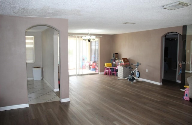 recreation room featuring dark wood-type flooring, a textured ceiling, and an inviting chandelier