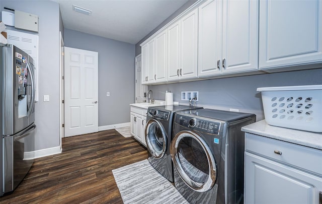 clothes washing area with cabinets, sink, washing machine and dryer, and dark hardwood / wood-style flooring