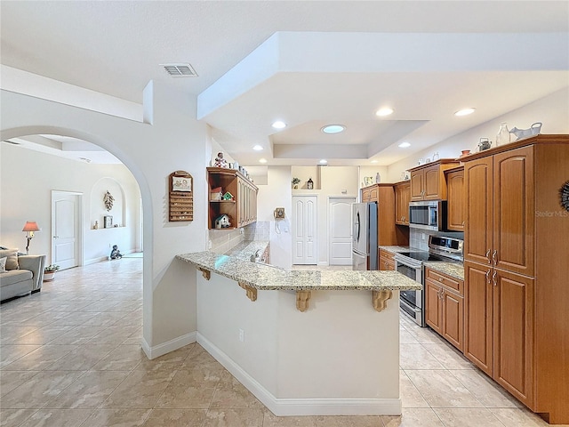 kitchen with a kitchen breakfast bar, tasteful backsplash, light stone counters, kitchen peninsula, and appliances with stainless steel finishes