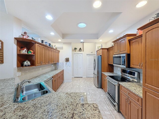 kitchen with sink, a raised ceiling, light stone counters, backsplash, and appliances with stainless steel finishes