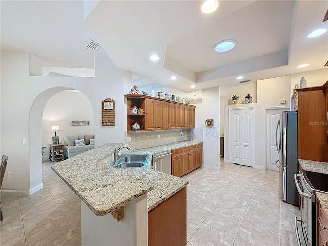 kitchen featuring backsplash, sink, light stone counters, kitchen peninsula, and stainless steel appliances