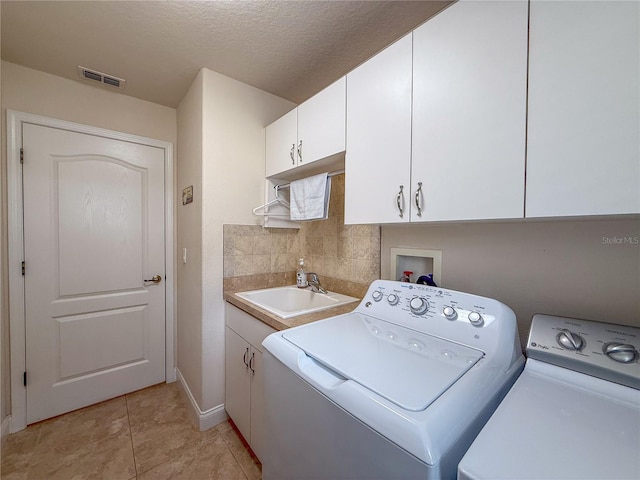 washroom featuring sink, cabinets, washing machine and dryer, a textured ceiling, and light tile patterned floors