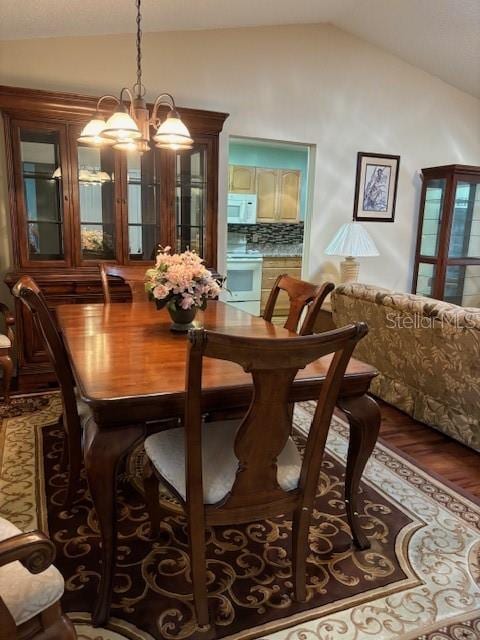 dining area featuring dark wood-type flooring, vaulted ceiling, and a chandelier