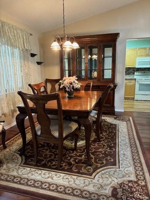 dining area with a notable chandelier, wood-type flooring, and vaulted ceiling