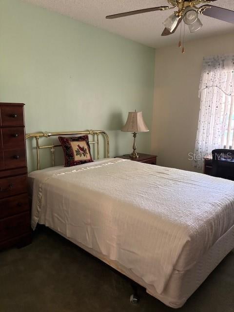 bedroom with ceiling fan, a textured ceiling, and dark carpet