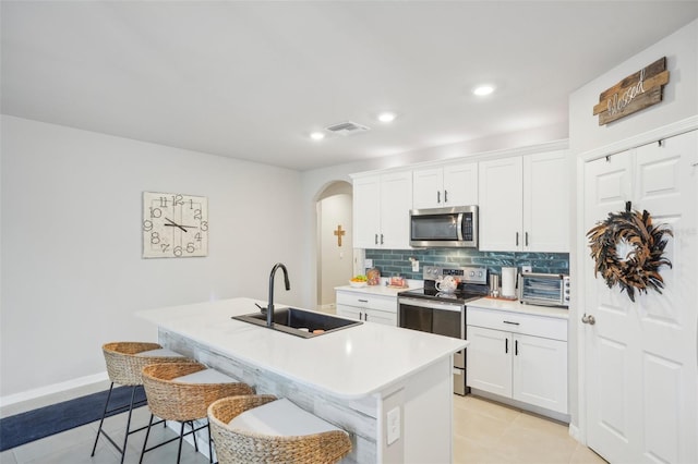 kitchen with white cabinets, appliances with stainless steel finishes, a kitchen island with sink, a kitchen bar, and sink