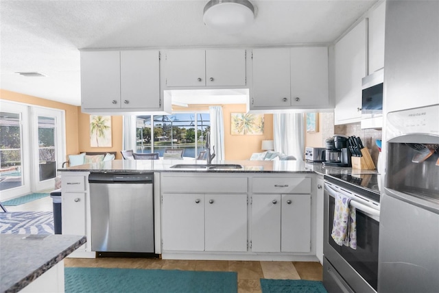 kitchen featuring light stone countertops, appliances with stainless steel finishes, kitchen peninsula, and white cabinets