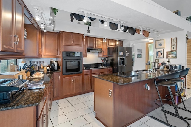 kitchen with dark stone countertops, black appliances, a breakfast bar area, and an island with sink