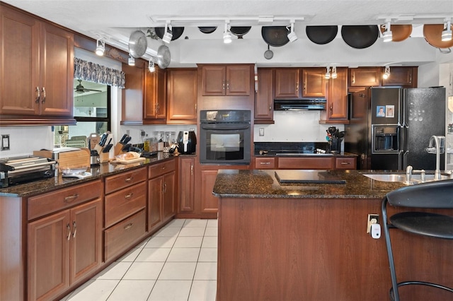 kitchen featuring black appliances, a center island, rail lighting, dark stone countertops, and light tile patterned floors