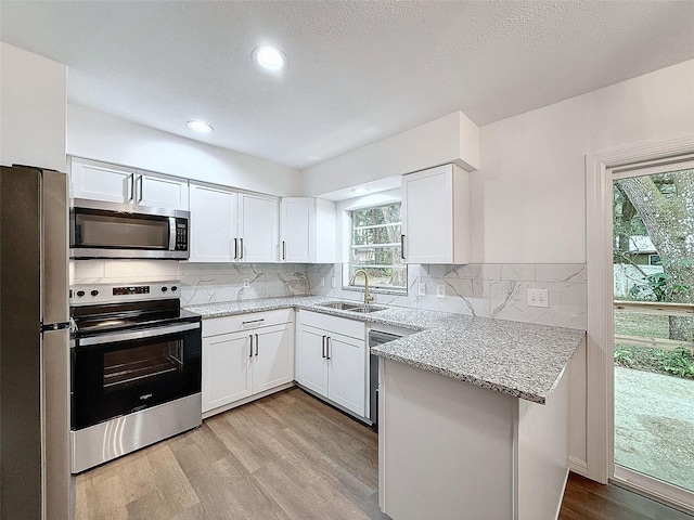 kitchen with sink, white cabinets, appliances with stainless steel finishes, light stone counters, and light hardwood / wood-style floors