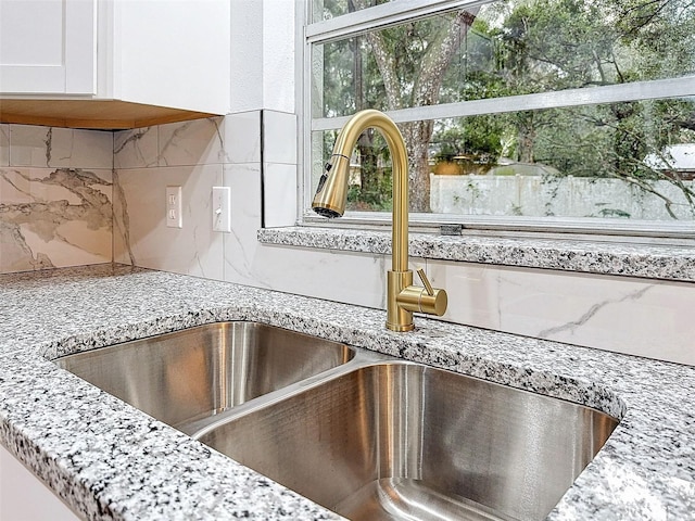 details featuring white cabinets, tasteful backsplash, sink, and light stone counters