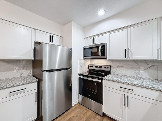 kitchen with white cabinetry, light hardwood / wood-style floors, appliances with stainless steel finishes, and backsplash