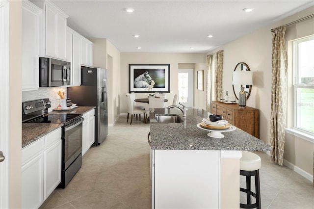 kitchen with dark stone countertops, a center island with sink, sink, white cabinetry, and appliances with stainless steel finishes