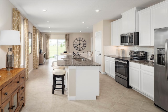 kitchen featuring white cabinetry, appliances with stainless steel finishes, dark stone counters, and an island with sink