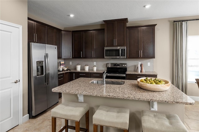 kitchen featuring a kitchen breakfast bar, an island with sink, sink, light stone countertops, and appliances with stainless steel finishes