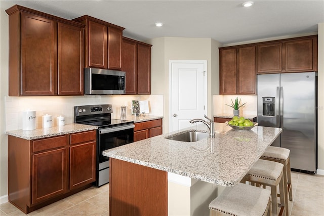 kitchen with an island with sink, a kitchen breakfast bar, light stone countertops, sink, and stainless steel appliances