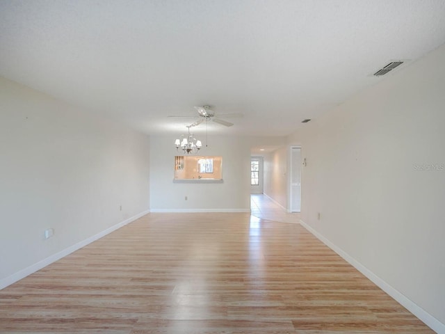 empty room with ceiling fan with notable chandelier, light wood-style floors, visible vents, and baseboards