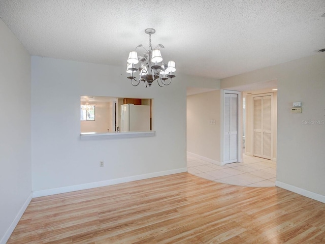 unfurnished room featuring wood finished floors, baseboards, a chandelier, and a textured ceiling