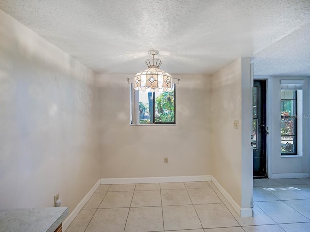 unfurnished dining area featuring light tile patterned floors, baseboards, and a textured ceiling