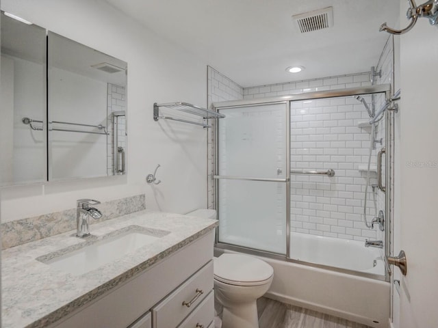 full bath with visible vents, bath / shower combo with glass door, toilet, wood finished floors, and vanity