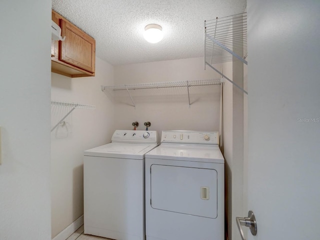 clothes washing area with cabinet space, a textured ceiling, and washing machine and clothes dryer