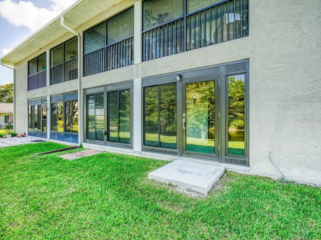 view of exterior entry with stucco siding and a lawn