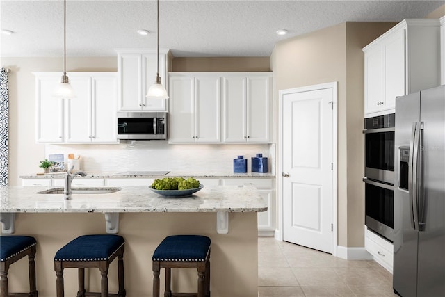 kitchen featuring light stone counters, white cabinetry, sink, pendant lighting, and stainless steel appliances