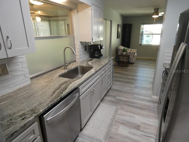 kitchen featuring tasteful backsplash, sink, light wood-type flooring, white cabinetry, and stainless steel dishwasher