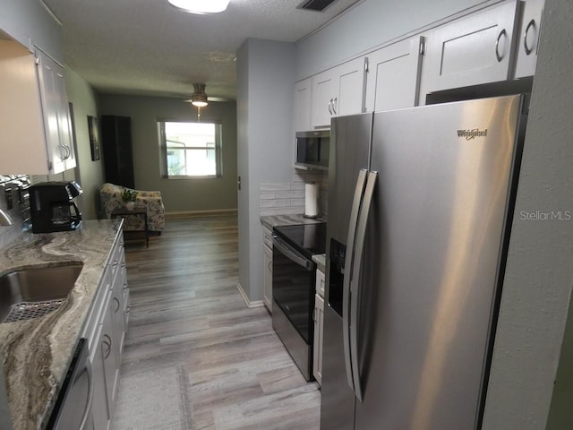 kitchen with light stone countertops, backsplash, stainless steel appliances, white cabinets, and light hardwood / wood-style flooring