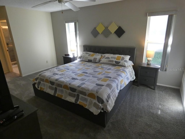 bedroom featuring multiple windows, ensuite bath, dark carpet, and ceiling fan