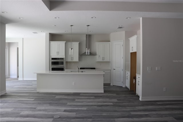 kitchen featuring wall chimney exhaust hood, recessed lighting, wood finished floors, and a center island with sink