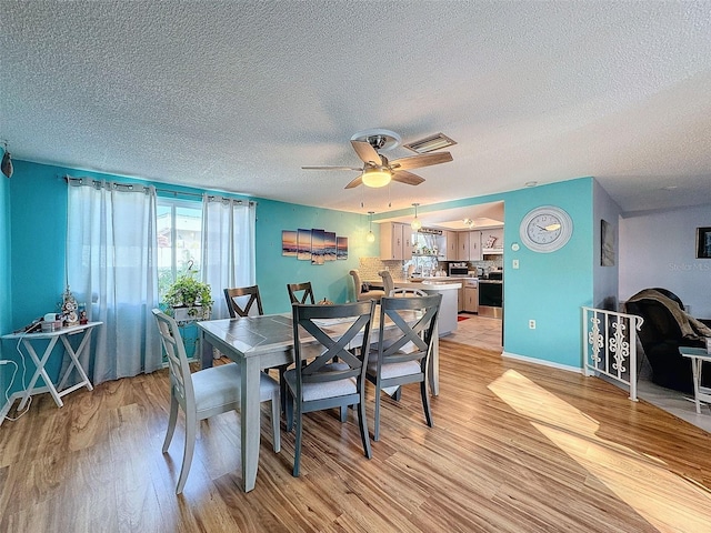 dining room with ceiling fan, a textured ceiling, and light wood-type flooring