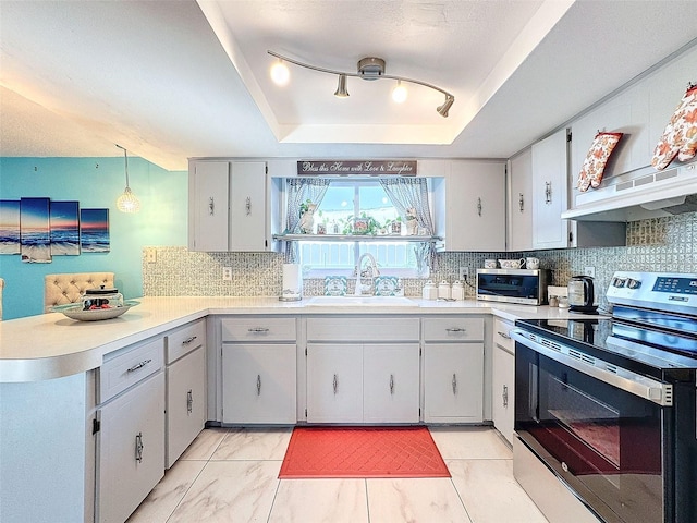 kitchen featuring stainless steel range with electric cooktop, backsplash, a tray ceiling, pendant lighting, and sink