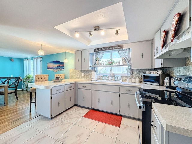 kitchen with kitchen peninsula, backsplash, a raised ceiling, sink, and stainless steel appliances