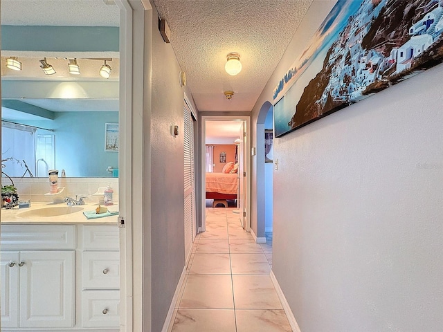 hallway featuring sink, light tile patterned flooring, and a textured ceiling