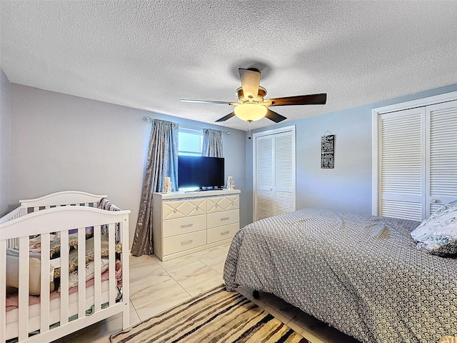 bedroom featuring multiple closets, a textured ceiling, light tile patterned floors, and ceiling fan