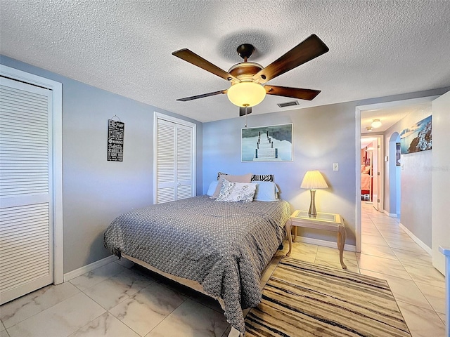 tiled bedroom featuring two closets, a textured ceiling, and ceiling fan