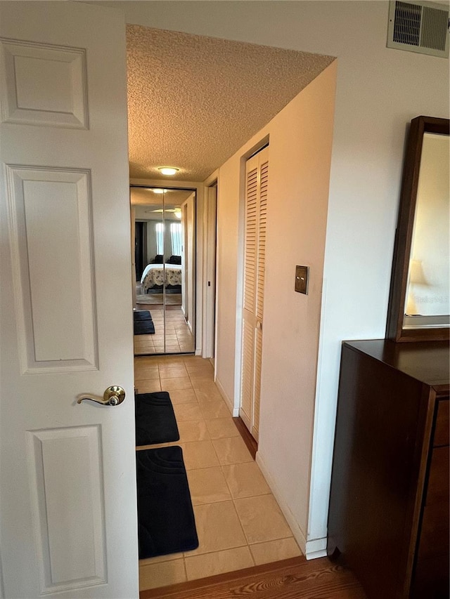 hall with a textured ceiling and light tile patterned floors