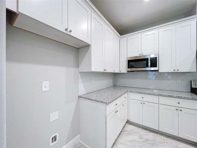 kitchen with marble finish floor, stainless steel microwave, white cabinetry, and light stone countertops