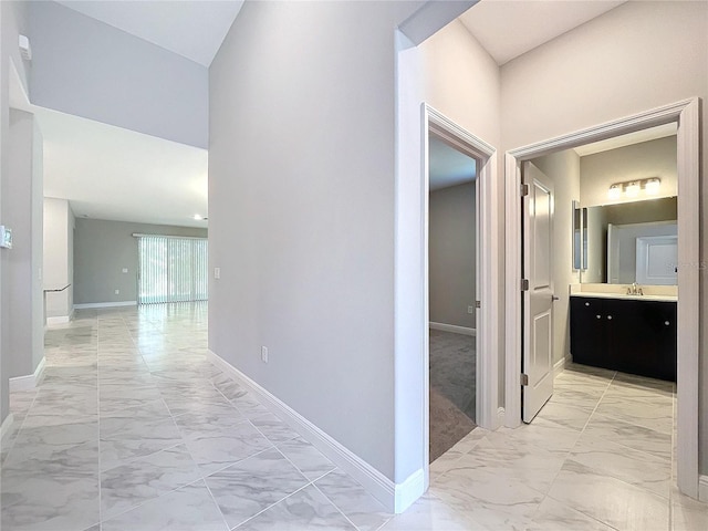 hall featuring a towering ceiling, marble finish floor, baseboards, and a sink