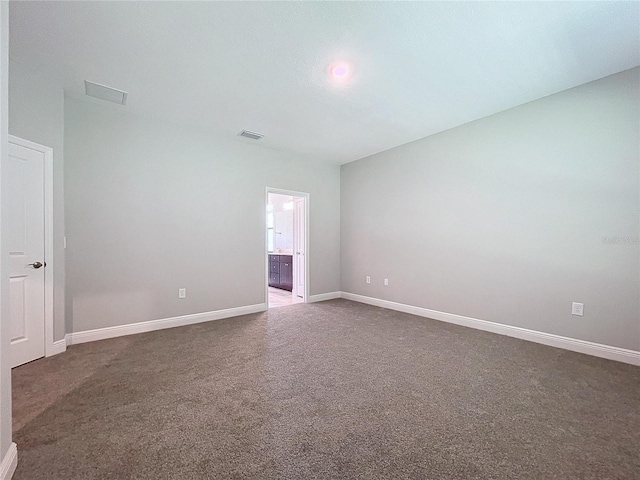 spare room featuring dark colored carpet, visible vents, and baseboards