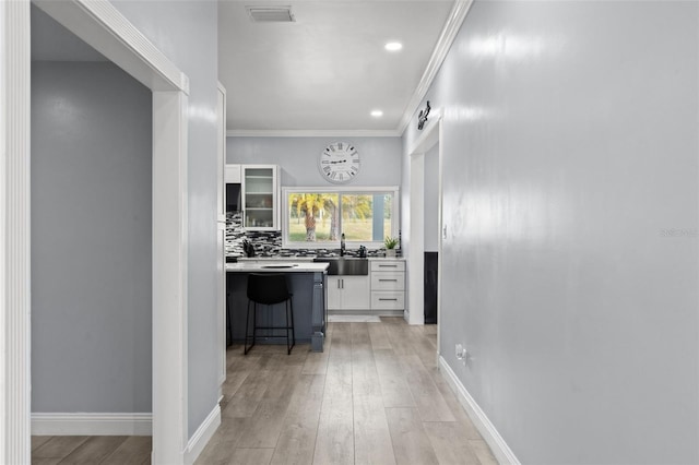 hallway featuring sink, light wood-type flooring, and crown molding