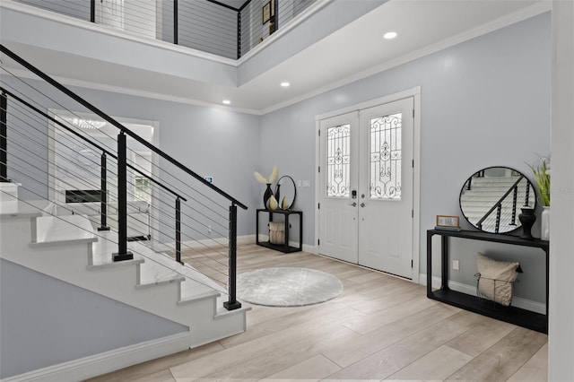 foyer entrance featuring a towering ceiling, crown molding, light hardwood / wood-style flooring, and french doors